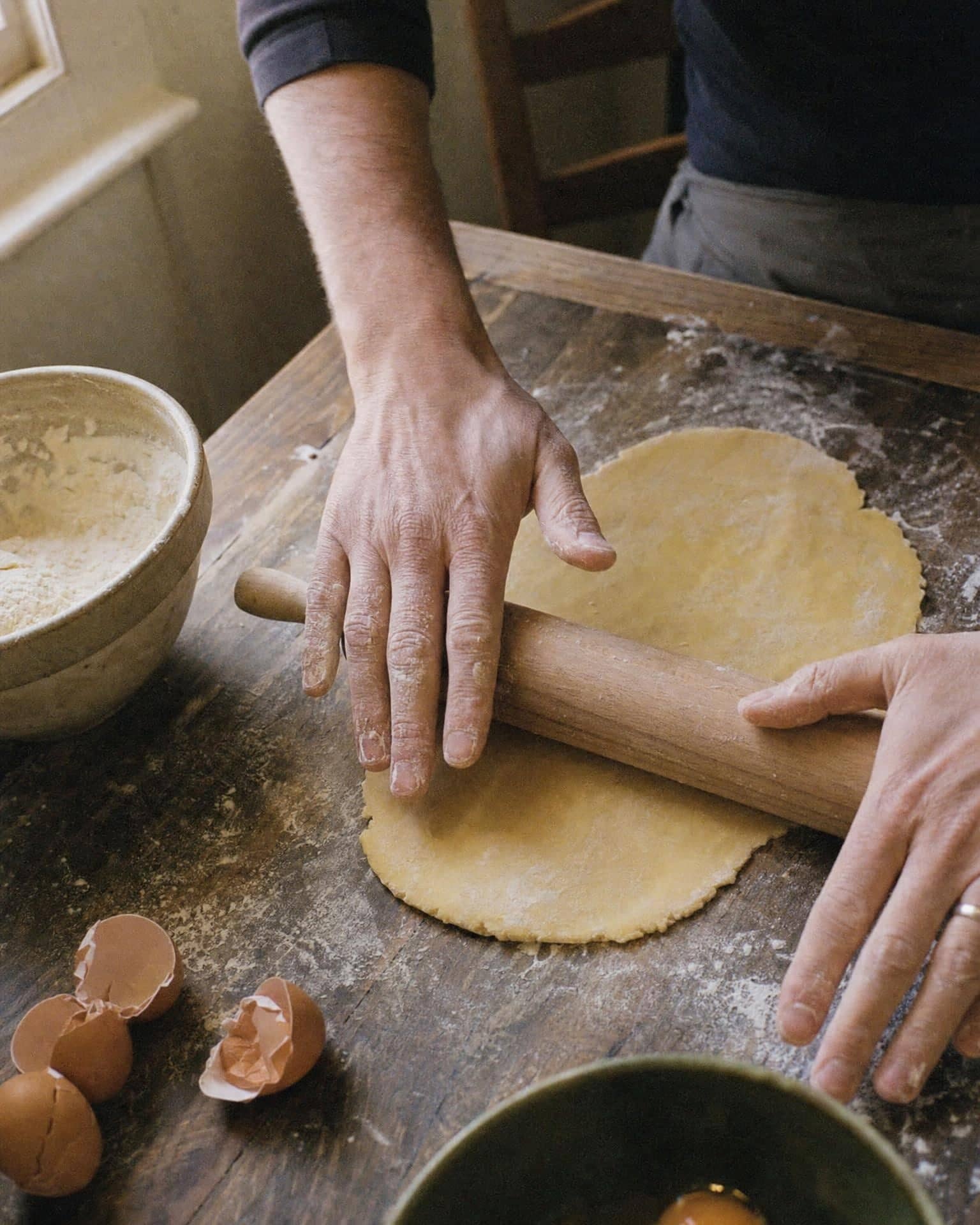 Hands rolling out fresh pasta dough on a floured kitchen table