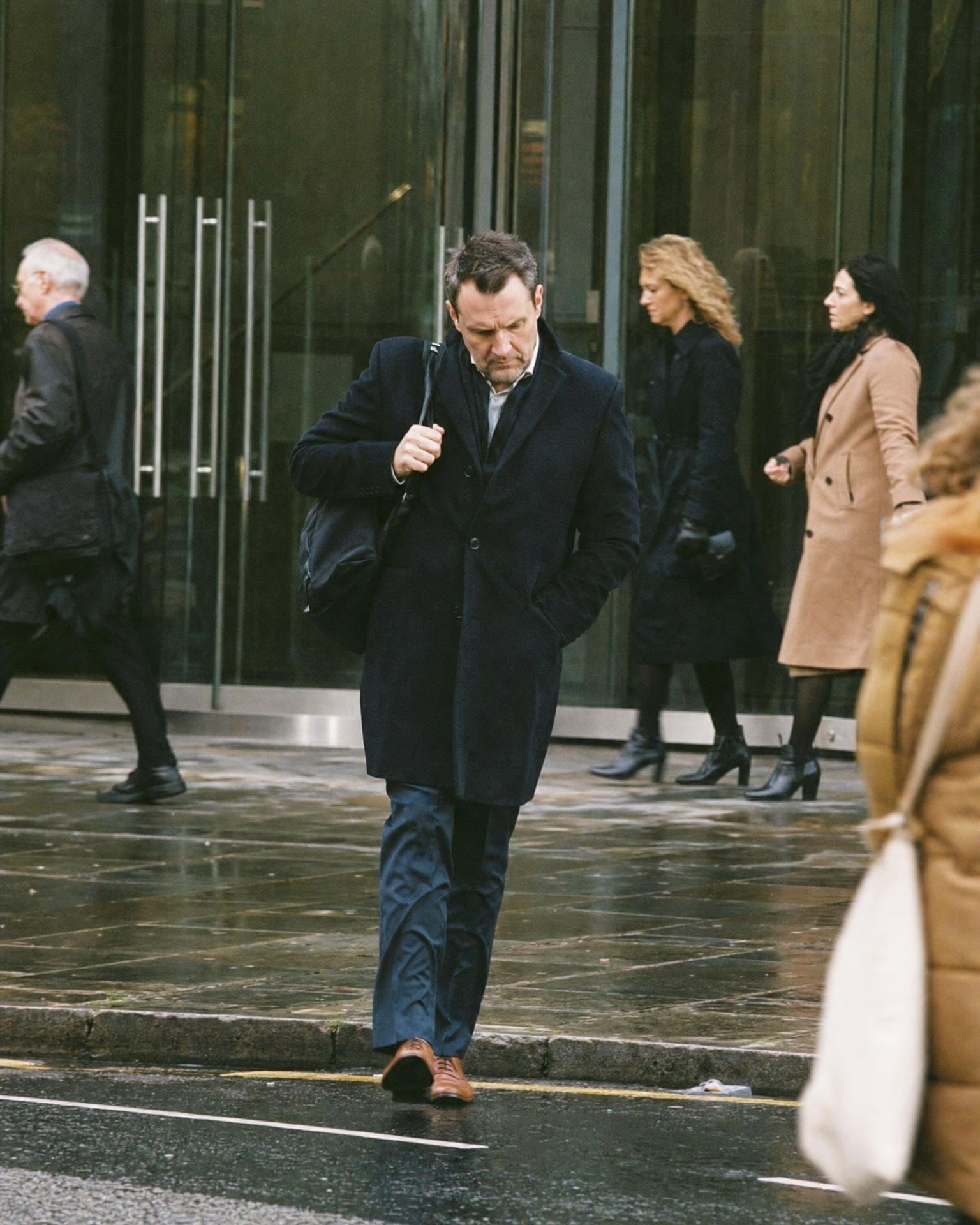 Ein Sales Director verlässt ein Bürogebäude auf dem Weg zum nächsten Termin und checkt sein Handy