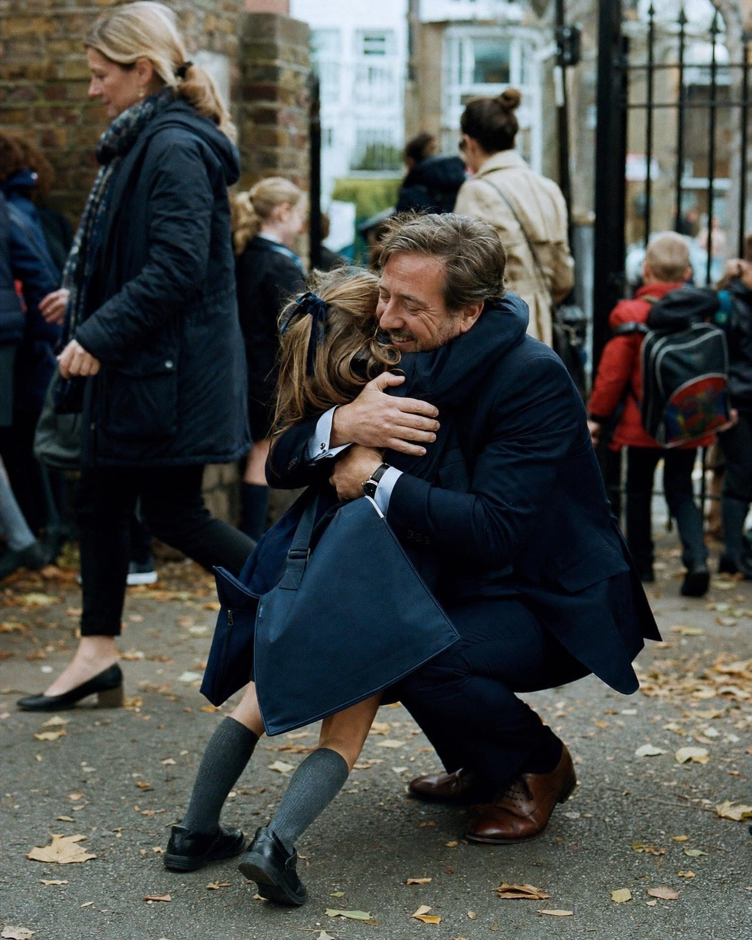 A father in a suit hugging his daughter at the school gate