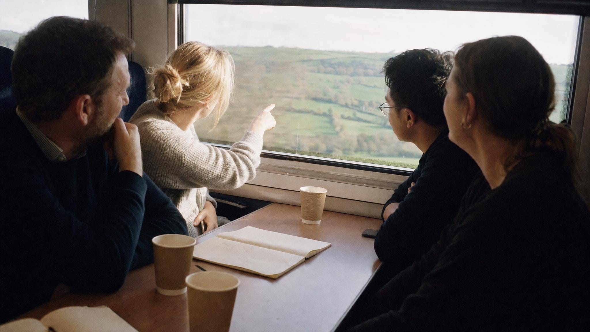Vier Kolleg:innen reisen gemeinsam im Zug durch die Landschaft