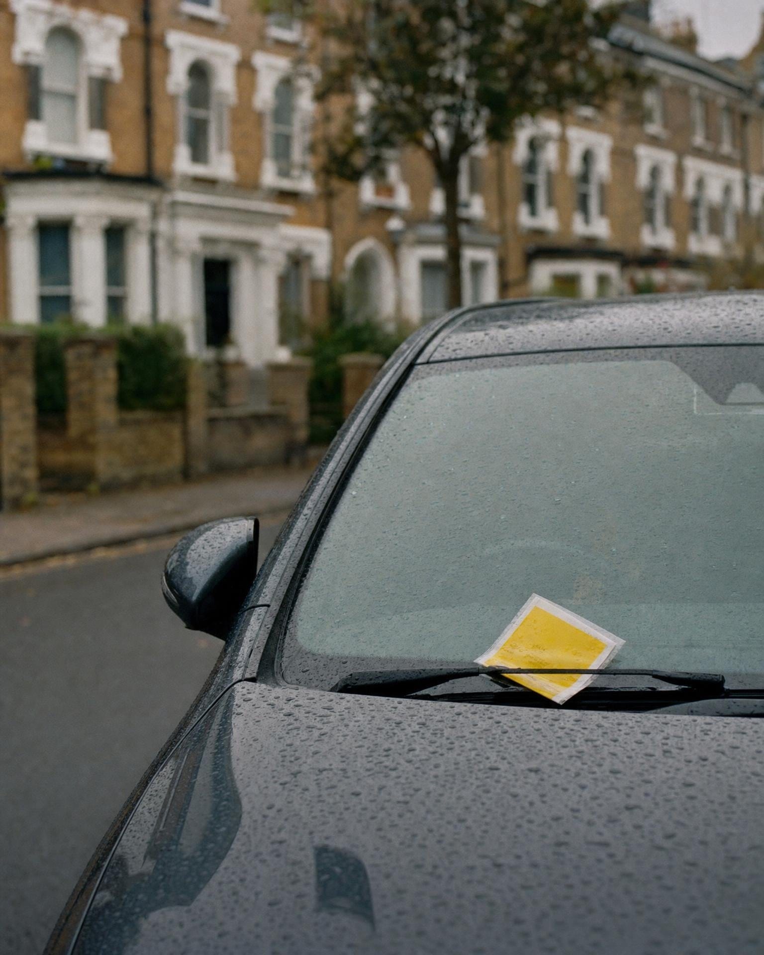 A parking ticket tucked under a car's windscreen wiper on a drizzly London street