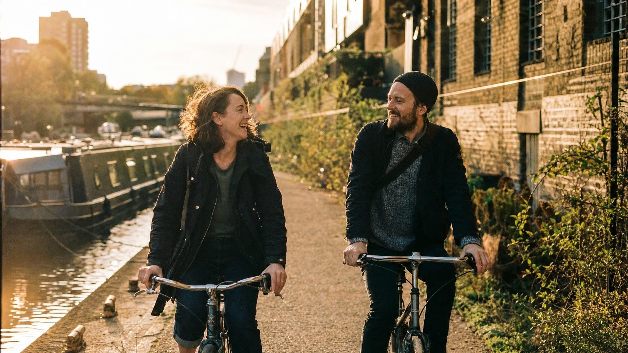 Zwei Kolleg:innen fahren in der Goldenen Stunde mit dem Fahrrad entlang eines Londoner Kanals nach Hause