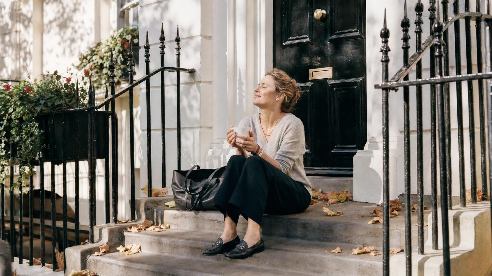 Eine Frau entspannt am Morgen in der Sonne auf den Stufen vor einem Londoner Townhouse