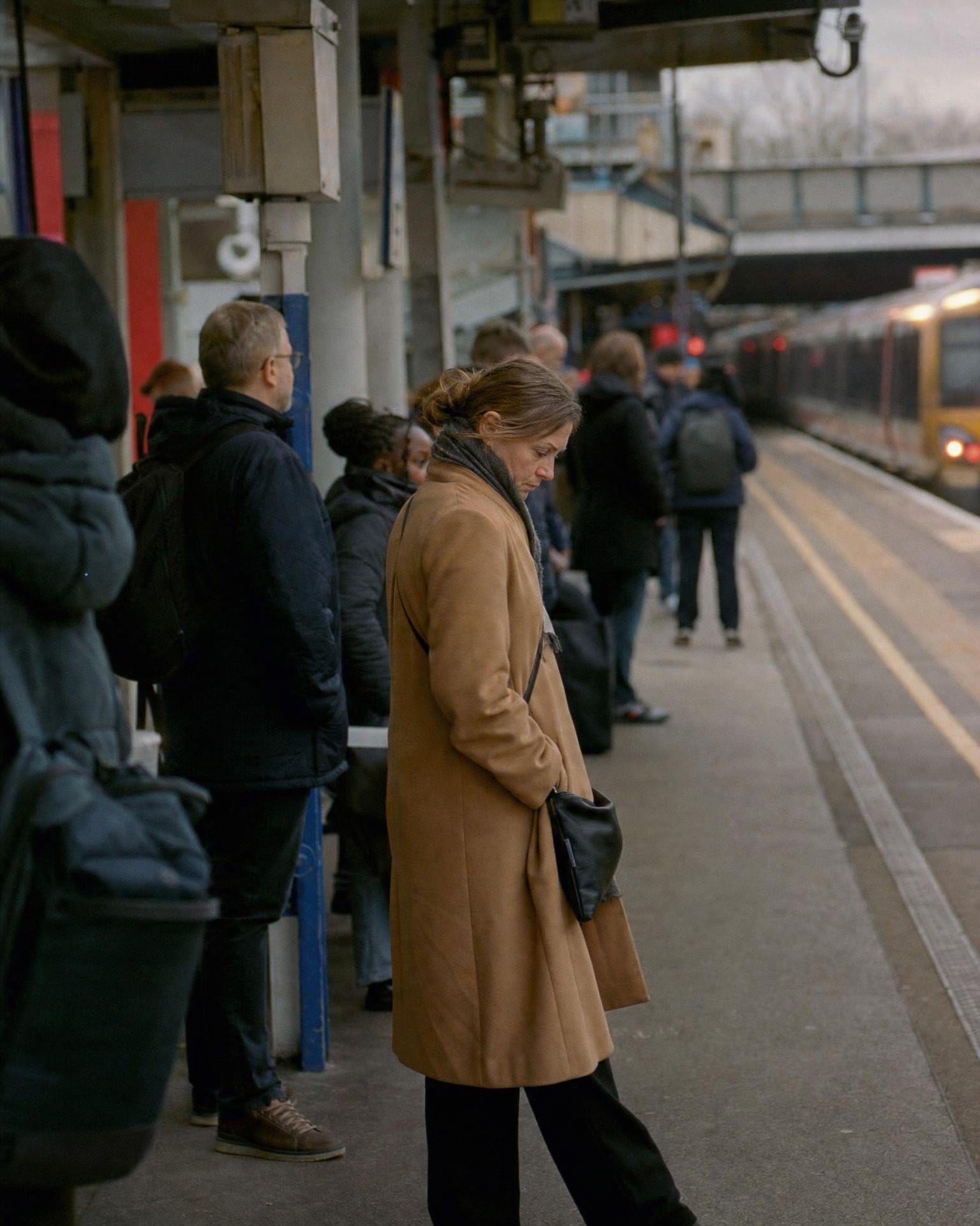 A commuter checks her phone on a station platform while a delayed train waits